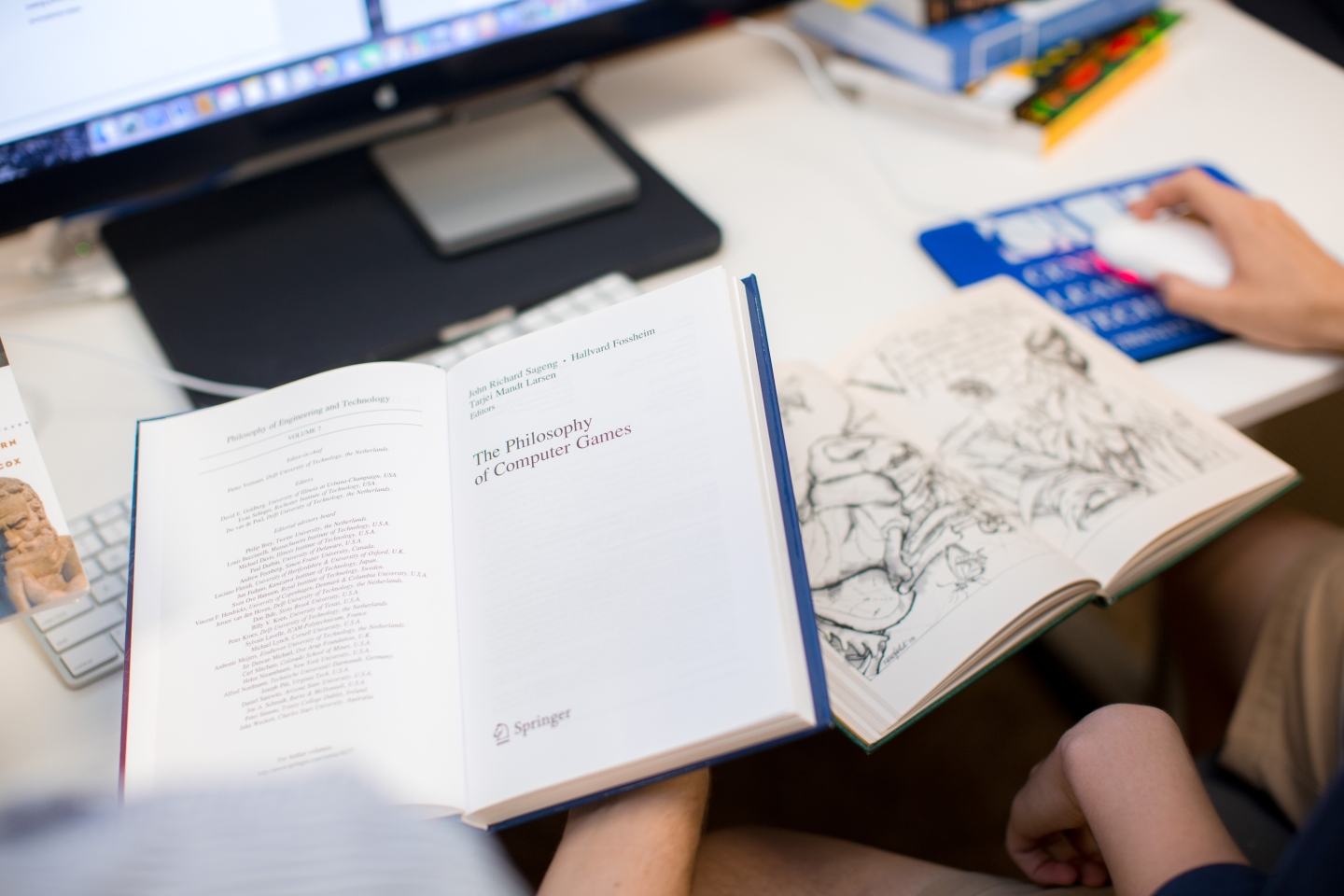 Two students reading books while using computer