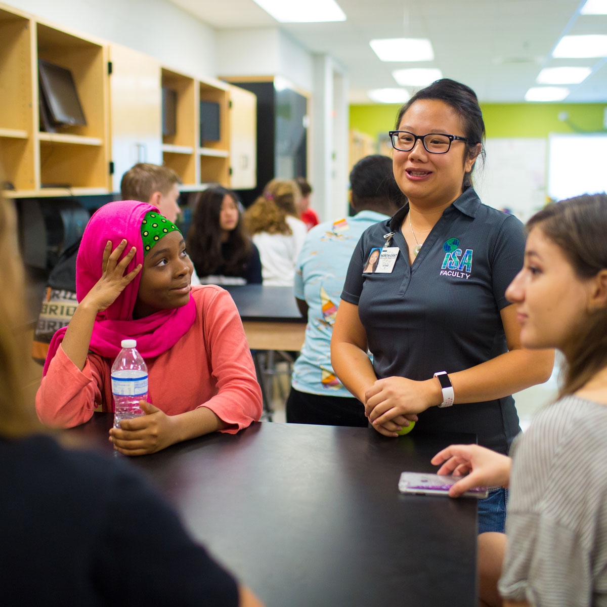a teacher speaks with three students in a middle school science lab