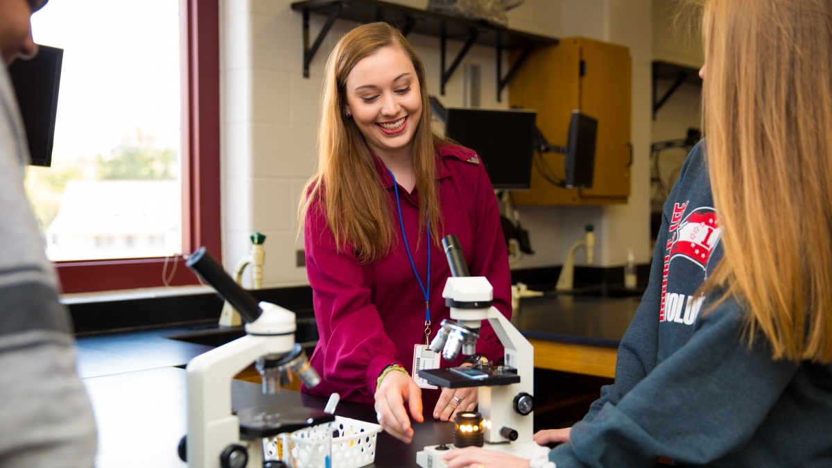 Trinity student showing a microscope to high school students