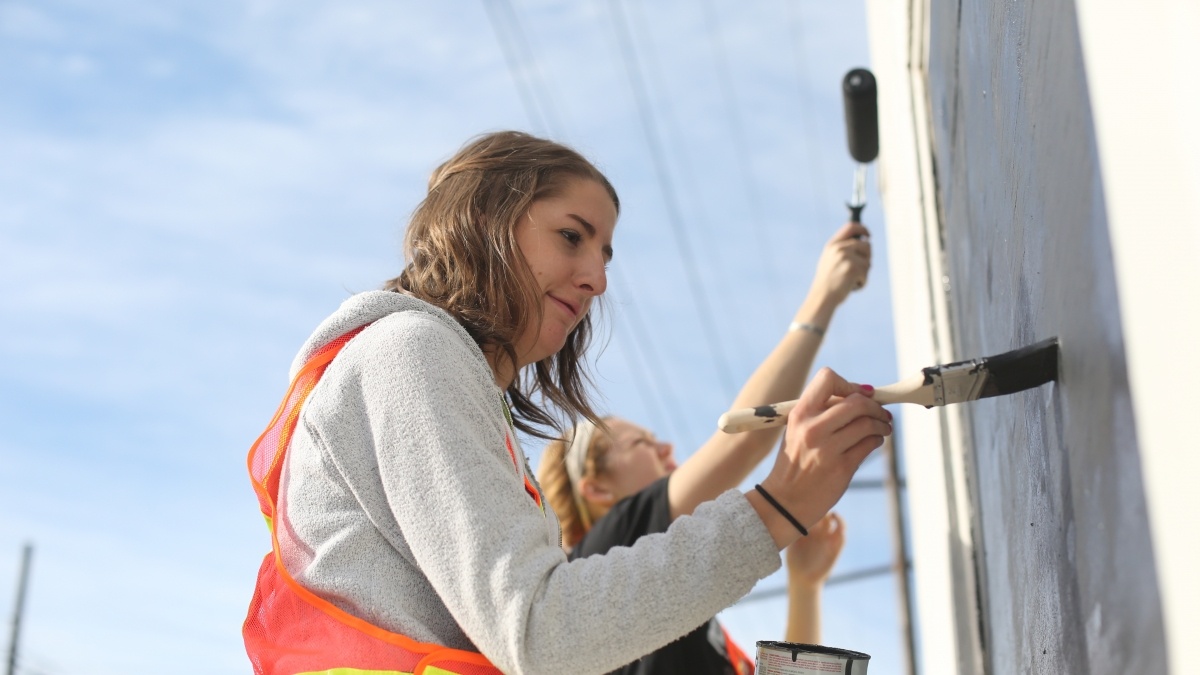 Students painting a pole white, while wearing safety vests