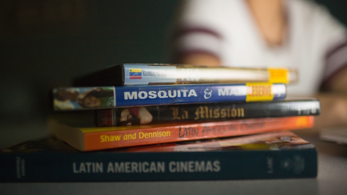 Stack of Spanish books on a table with student in the background 